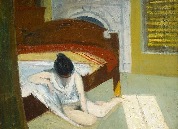 Young woman sits half naked on the floor next to a bed in a darkened room.