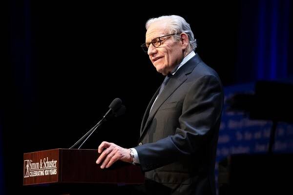 Bob Woodward speaks at a podium against a darkened background. 