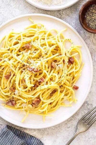 Spaghetti carbonara with pancetta served on a white plate.