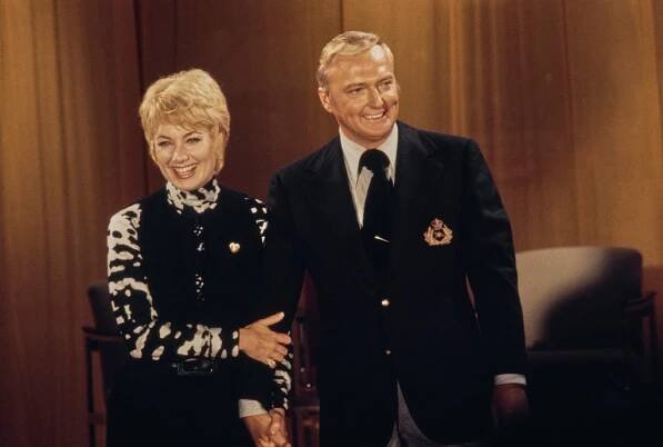 Shirley Jones, wearing a black-and-white outfit beneath a black waistcoat, holding hands with her husband Jack Cassidy, who wears a dark blue blazer with an emblem on the left breast pocket over a striped shirt with a black tie, August 1971.