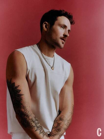 portrait of a person with tattoos wearing a sleeveless top against a pink background