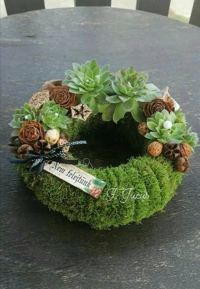 a moss wreath with pine cones and succulents sits on a wooden table