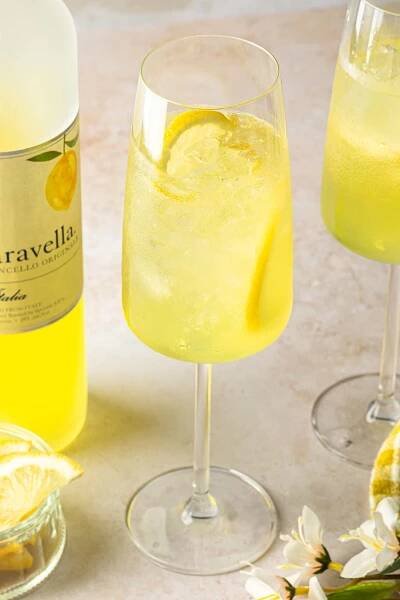 Close up of a limoncello spritz in a glass with ice and lemon wheels. 