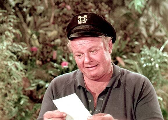 Person in a captain's hat and casual shirt, reading a paper outdoors, surrounded by foliage