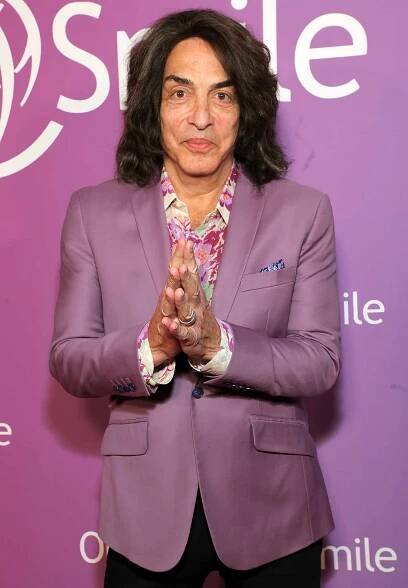 An individual gestures with hands clasped on a purple background at an Operation Smile event