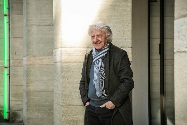 Emil Steinberger wird im Januar 92 Jahre alt. Er lächelt, trägt Schal und Mantel und steht vor Säulen im Bistro des Kunstmuseums Basel.