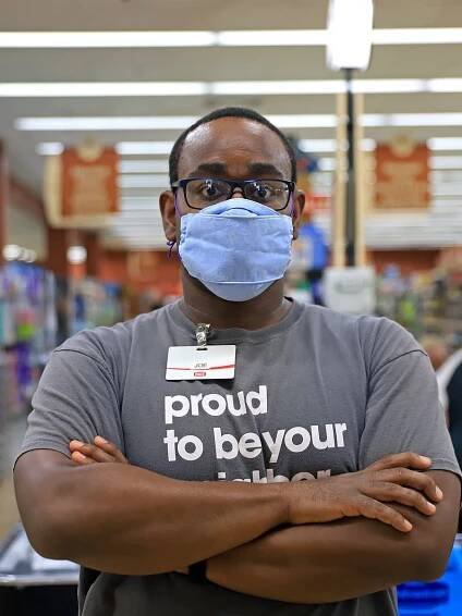 Photograph of essay author Joseph Vernon Smith. He is a Black man standing with his arms crossed looking at the camera. He wears a face mask and a Giant Eagle staff t-shirt that says proud to be your neighbor.