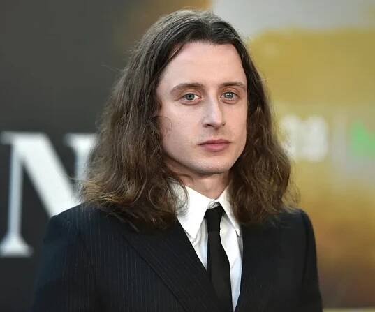 A person with long hair in a suit and tie at a formal event.
