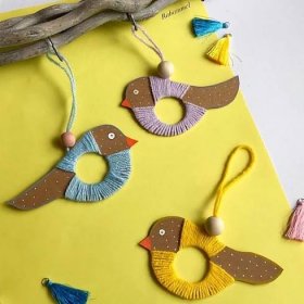 three birds are hanging from a branch on a yellow surface with other ornaments around them