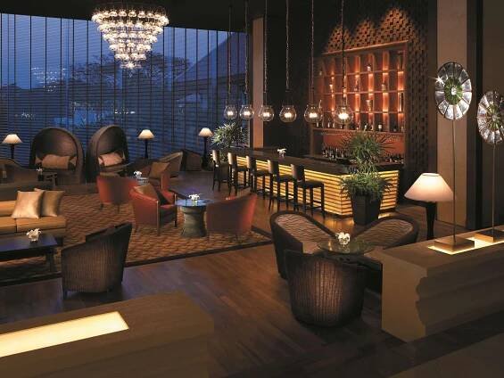 Shangri-La Chiang Mai Exterior photo The photo shows a stylish and dimly lit lounge area, likely in a hotel or upscale establishment, at dusk or night. The space is designed with a warm and inviting ambiance, featuring a mix of comfortable seating and a well-stocked bar.

In the foregro