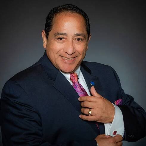 Professional man in a dark suit with a pink tie posing confidently.