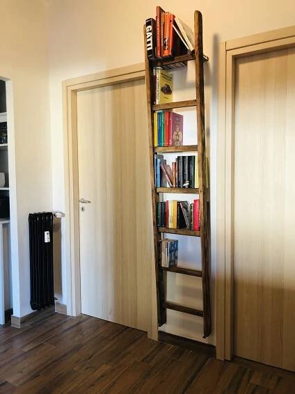 a bookshelf in the corner of a room with wooden flooring and white walls