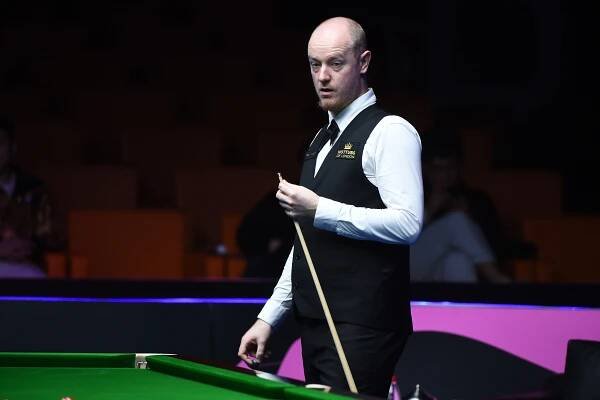 a man holding a cue next to a pool table with a vest that says masters snooker on it