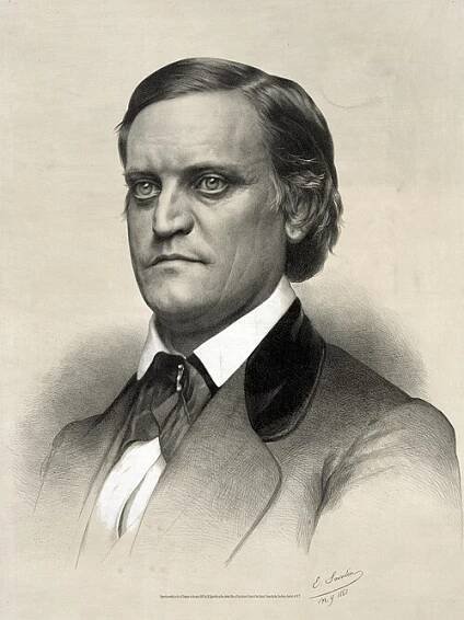 A man with dark hair and large, round eyes wearing a high-collared white shirt, black jacket, and black tie