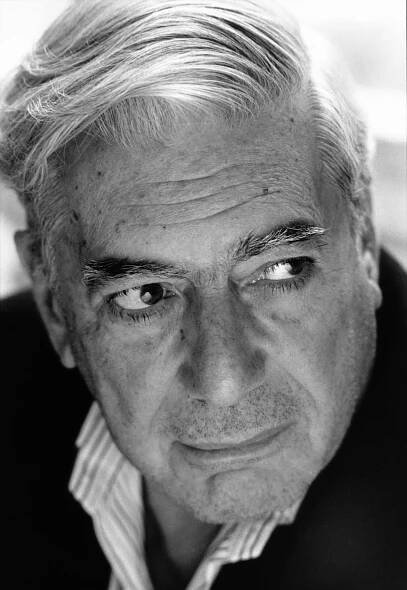 This black-and-white portrait of Mario Vargas Llosa shows him in a striped button-down shirt open at the collar, looking to the right side of the frame with his white hair swept back from his forehead.
