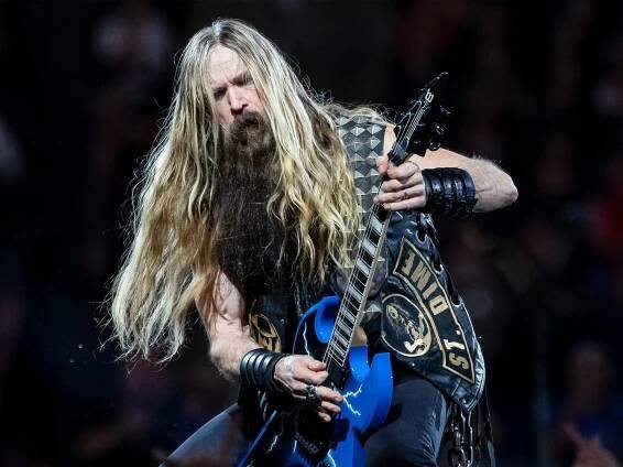 Zakk Wylde captured playing guitar on stage. His guitar is blue and covered with lightning bolts. He has long hair and a beard.