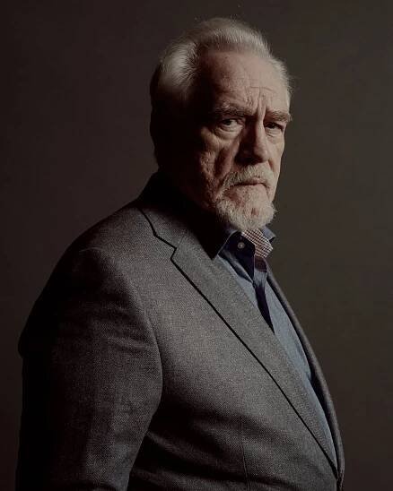 A white-beared, stern looking, bushy-browed man in a gray jacket glowers at the camera.