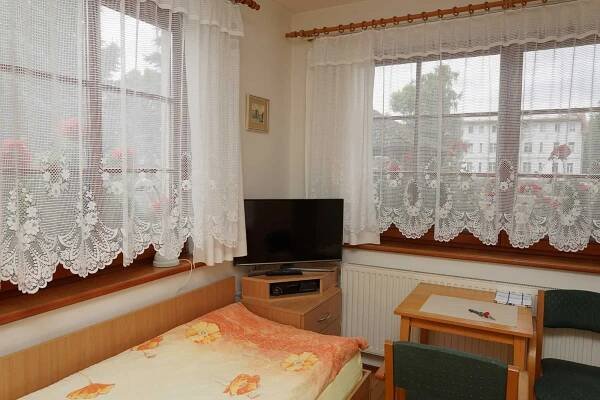 a small room with a bed and a tv and windows at Penzion u lázní in Velké Losiny