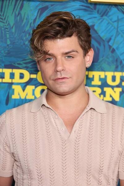 Person with styled hair wearing a textured short-sleeve shirt, standing against a patterned blue and yellow background