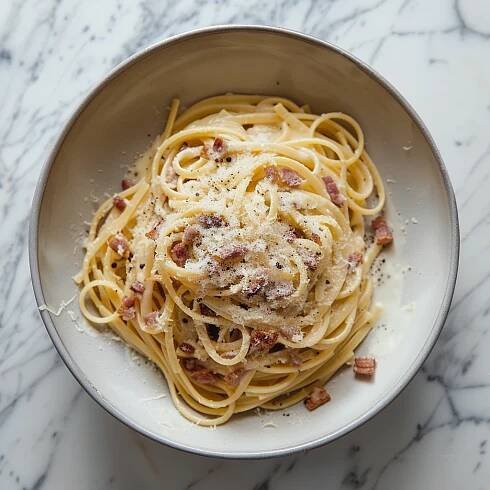 A bowl of freshly made Spaghetti Carbonara topped with grated Parmesan cheese, featuring strands of spaghetti coated in a creamy sauce made from eggs and cheese, with crispy pieces of pancetta or guanciale, garnished with a sprinkle of freshly ground black pepper.