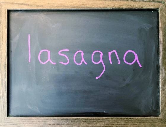 Word 'lasagna' written on a chalkboard with a purple chalk marker.