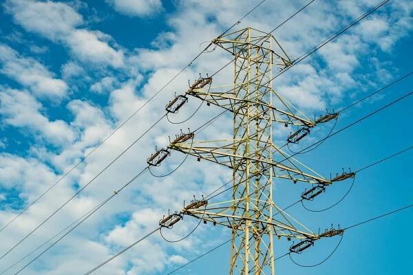 Free A tall electrical transmission tower stands against a backdrop of blue sky and white clouds. Stock Photo