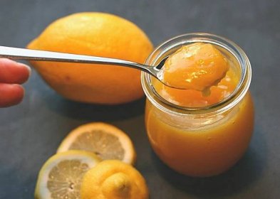 A delicious spoonful of creamy and tangy lemon curd, with a fresh lemon, lemon slices and the jar of lemon curd in the background