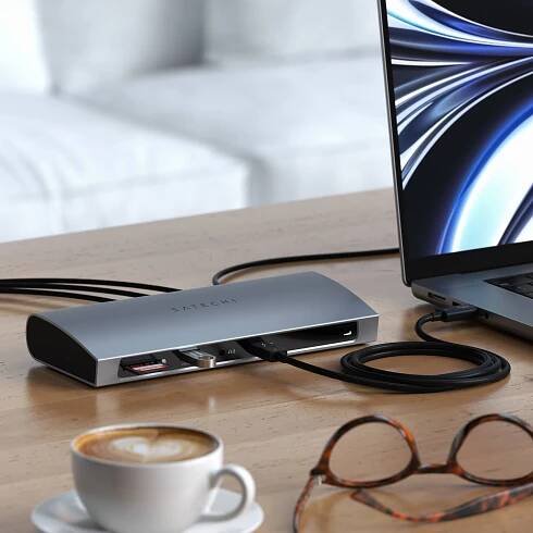 Close-up view of a Satechi Thunderbolt 4 Dock in use, showing a flash drive, SD card, and Thunderbolt cable connected to its various ports. The dock is actively linked to a MacBook, visible in the background.
