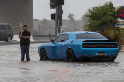 A man stands in floodwaters next to a blue car