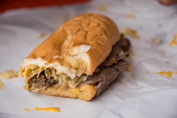 Half eaten beef sandwich in a long sandwich roll on a piece of paper