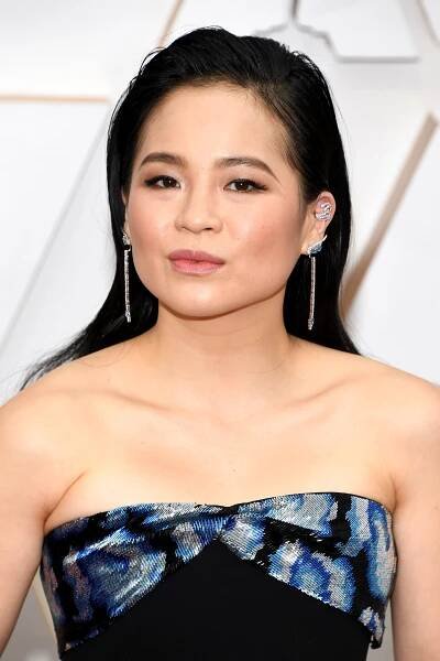 Kelly Marie Tran wearing a strapless dress with a patterned top and long earrings, posing on a formal red carpet