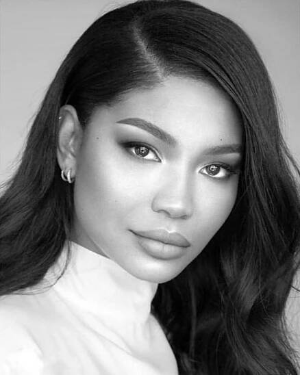 Black and white portrait of a woman with striking eyes and full lips, resembling We Love Her Dresses…How To Dress Like Chanel Iman, styled in a white high-collar blouse. Her dark hair is smoothly styled, and she