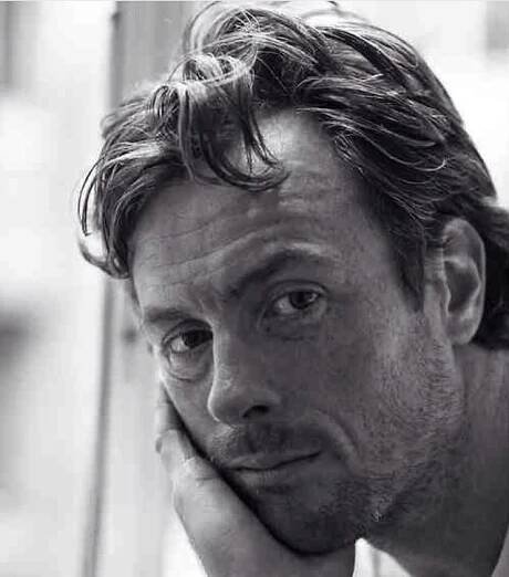 a black and white photo of a man with his hand on his chin looking at the camera