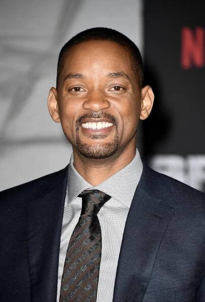 Will Smith smiling at an event, wearing a formal suit and tie