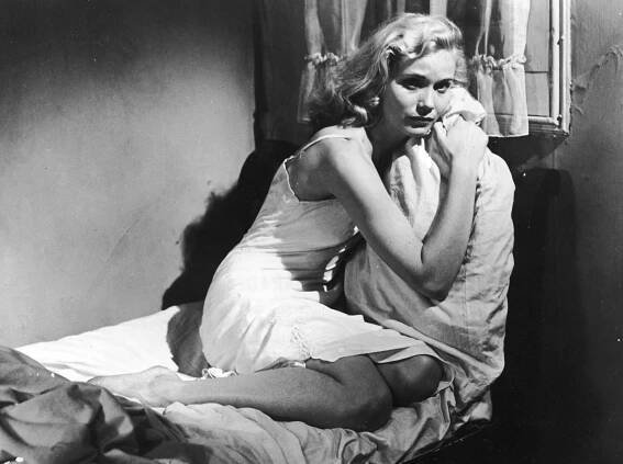 American actor Eva Marie Saint sits on a bed and clutches a pillow in a still from the film, 'On The Waterfront,'