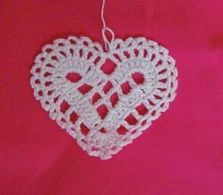a white crocheted heart hanging on a pink background with the word love written across it