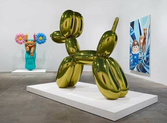 Golden balloon dog stands in the middle of room.