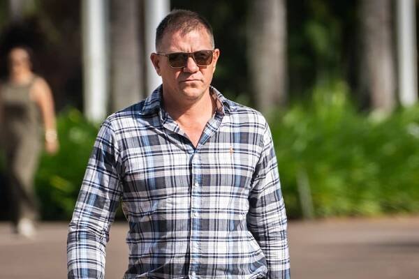 A man wearing a chequered shirt and sunglasses walking.