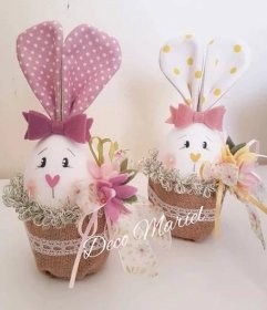 two stuffed rabbits in baskets with bows on their heads, one is pink and the other is white