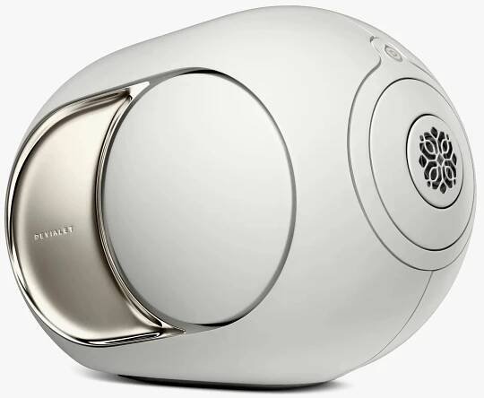 A sleek, modern white speaker with a rounded, futuristic design. It features a large circular driver on the side and a metallic accent plate with the brand name "Devialet" engraved on it. The speaker has a smooth, glossy finish and a small, intricate grille on the front.