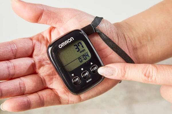 A person points to a button on the Omron Walking Style IV Pedometer