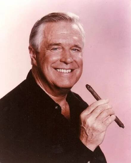 an older man holding a pen and smiling at the camera while wearing a black shirt