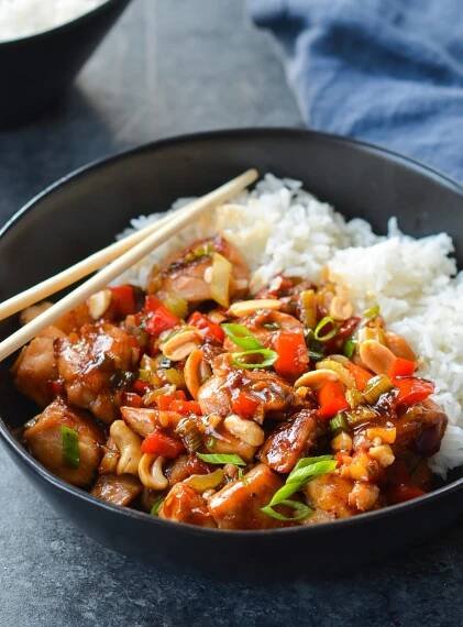 Chopsticks on a bowl of Kung Pao chicken with rice.