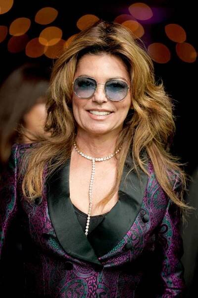 Shania Twain wearing blue sunglasses, a diamond necklace, and a blue and purple blazer