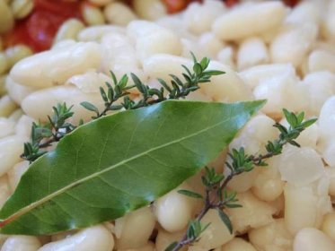 A close up image of haricot beans with a bay leaf and a couple of sprigs of thyme.