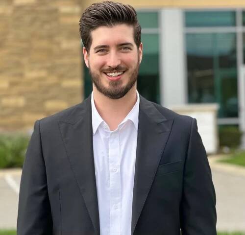 Jackson Dale in a suit and white shirt is smiling in front of a building .