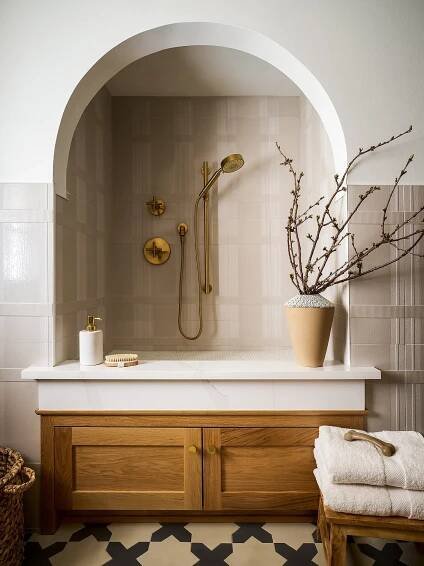  A cozy bathroom with a built-in shower alcove, brass fixtures, and natural wood cabinetry, accented by soft beige tiles and organic textures. 