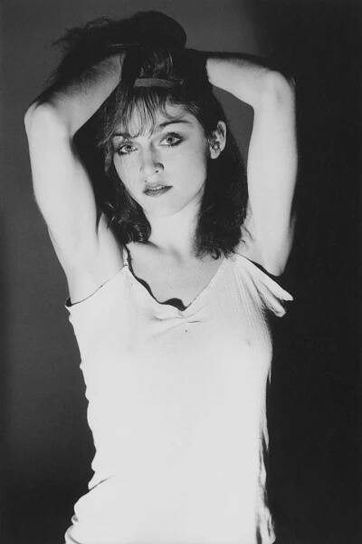 A person poses with arms raised, wearing a casual sleeveless top, striking a confident and stylish pose