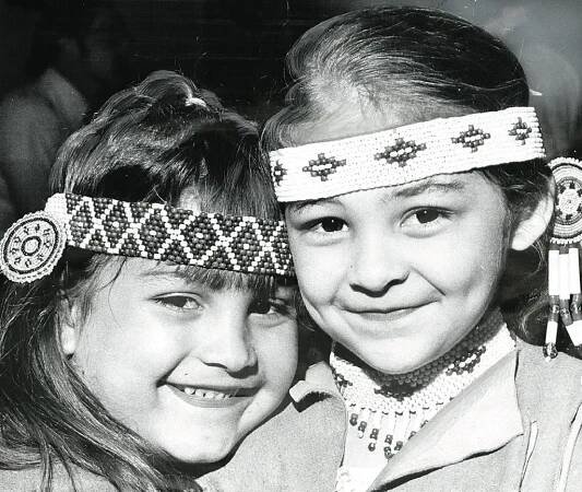 Two young Lumbee girls smile, wearing beaded headbands.