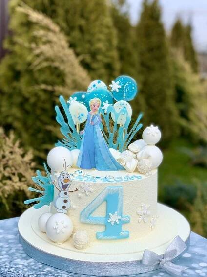 a frozen princess birthday cake with balloons and snowflakes on the top, sitting on a table outdoors